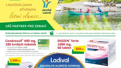 Rodina na zelené kanoi pádluje po jezeře u chaty s dřevěnou terasou, v pozadí loďky a stany v kempu